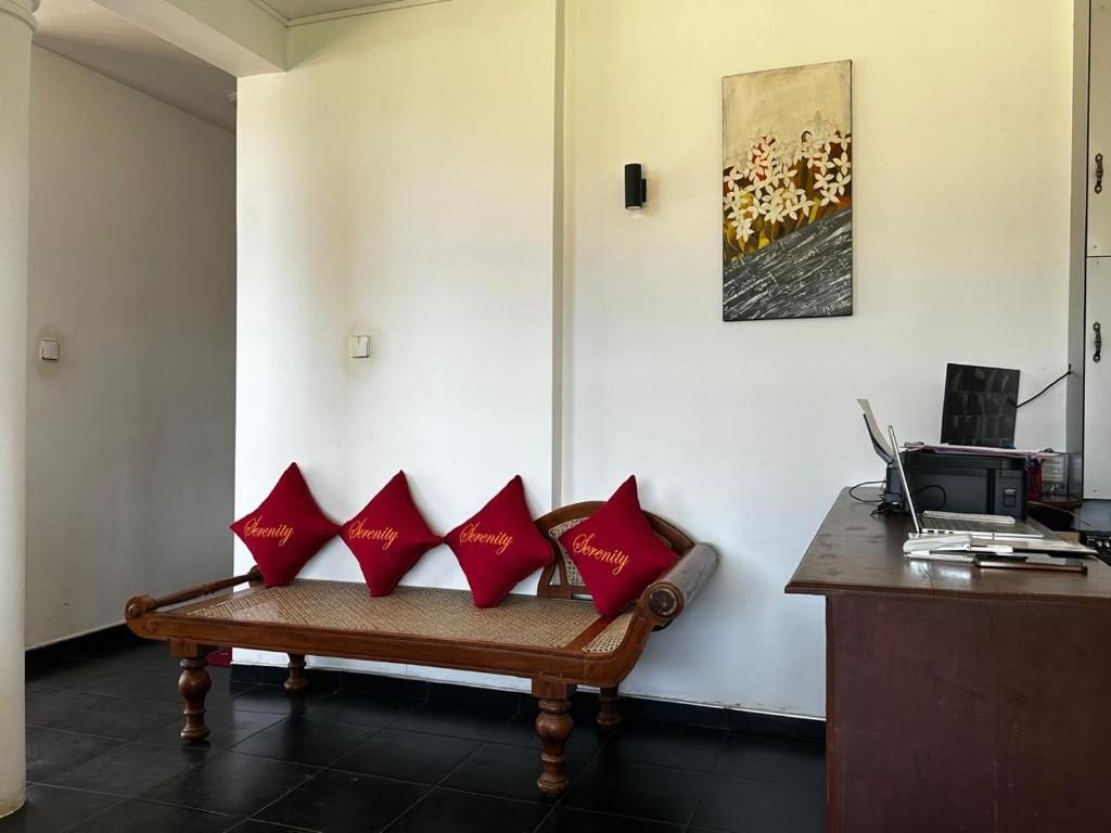 A wooden bench with red cushions, a painting on the wall, and a desk with a laptop.