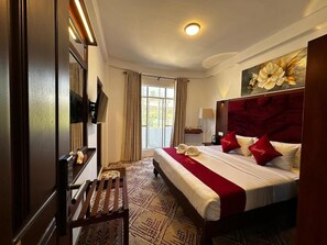 Hotellihuone, jossa on suuri sänky, puinen penkki, työpöytä ja näkymä ulos.
