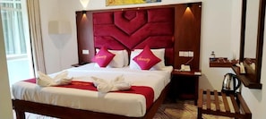 Habitació d'hotel amb un llit gran, dos coixins amb la paraula 'Serenity', una taula de nit amb una làmpada i una petita estant amb objectes.