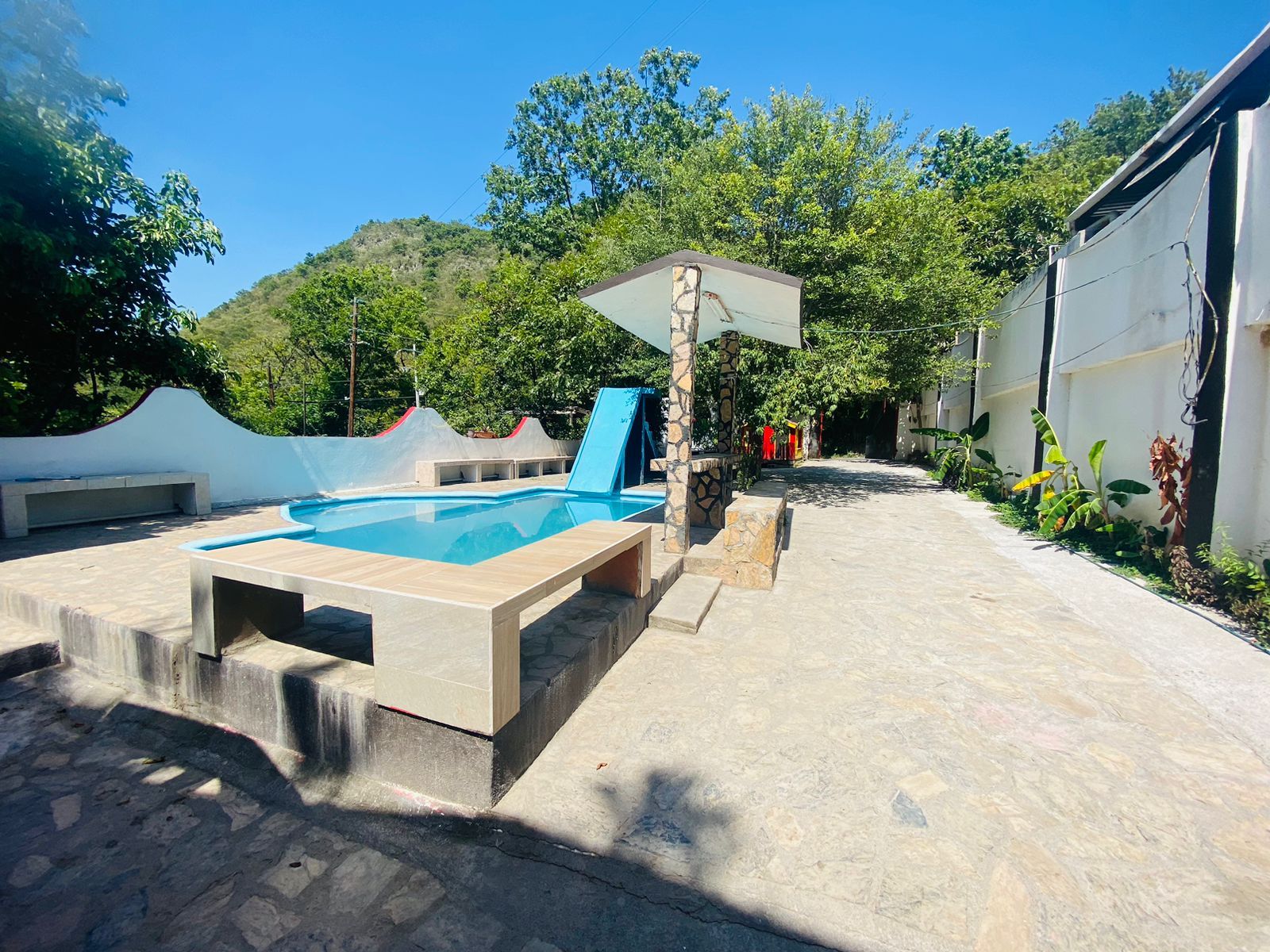 A swimming pool with a stone deck, a shaded area, and a view of a hillside.