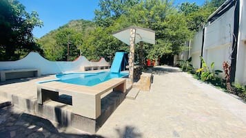 A swimming pool with a stone deck, a shaded area, and a view of a hillside.