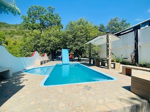 A swimming pool with a stone deck, surrounded by trees and a covered area with stone pillars. - New Listing (Santiago)