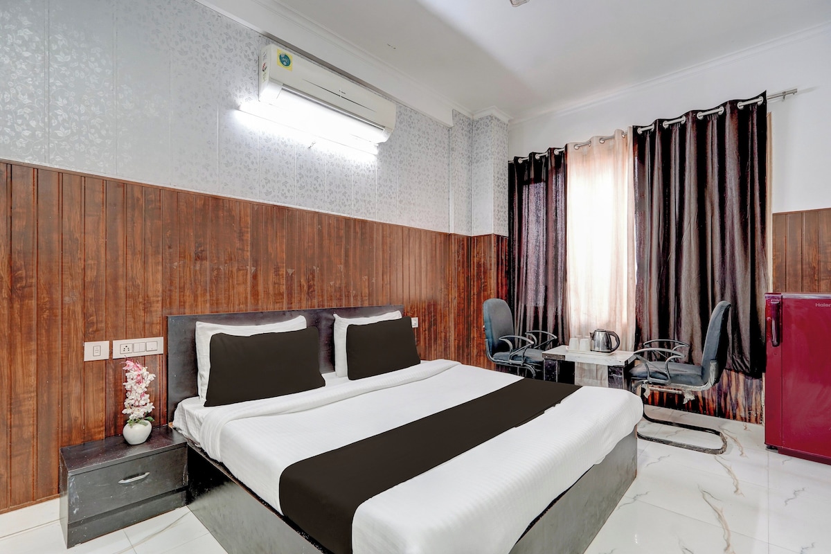 Una habitación de hotel con cama, mesita de noche, silla, escritorio y un refrigerador rojo.