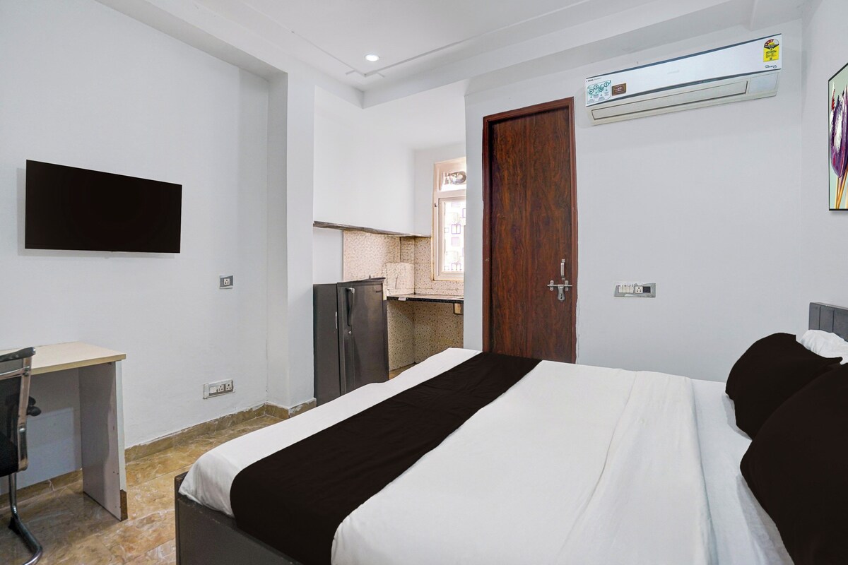 A hotel room with a bed, a desk, a wardrobe, an air conditioning unit, and a view of the outside.