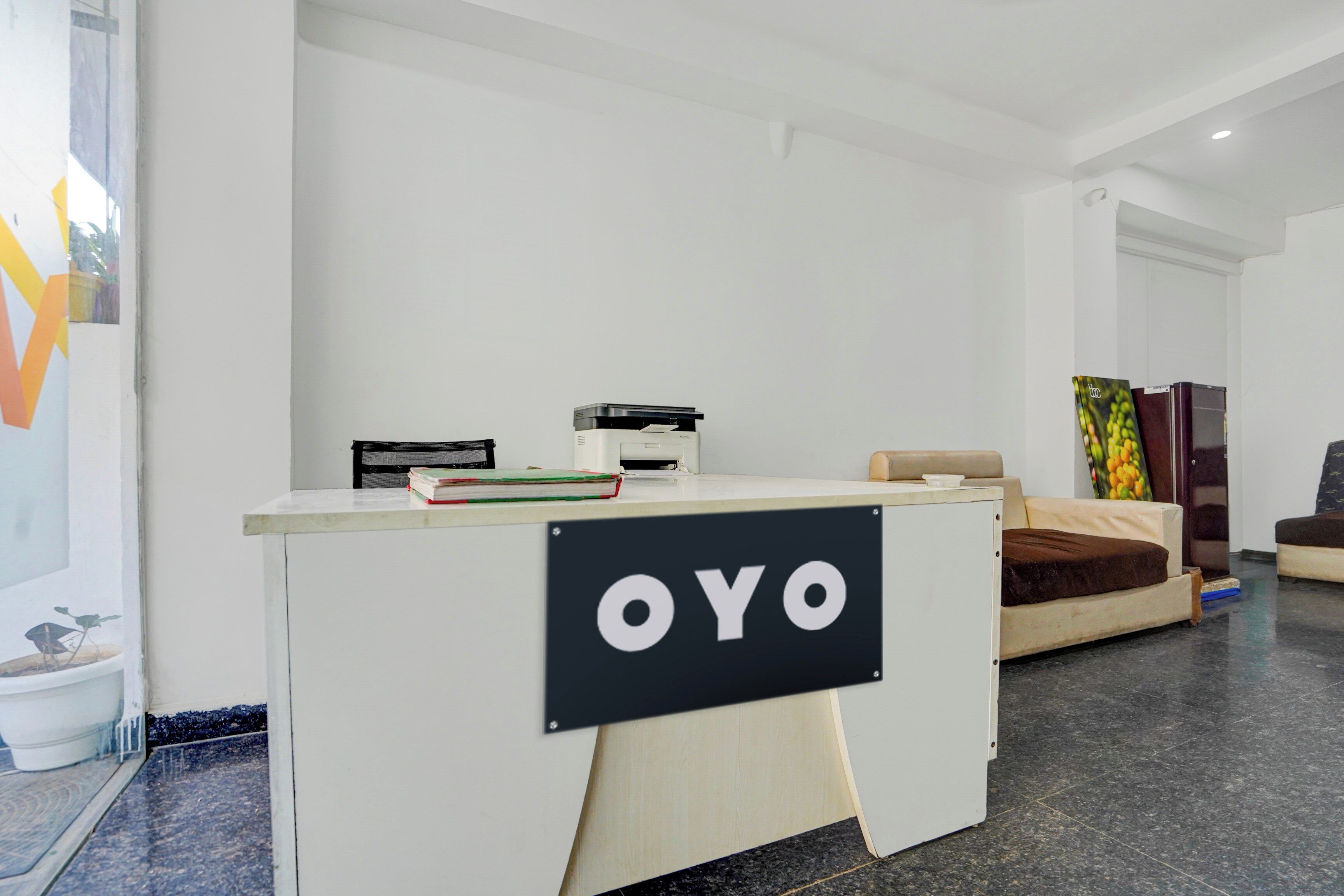 A reception desk with a sign that reads 'OYO' in a modern hotel lobby with a sofa and a painting in the background.