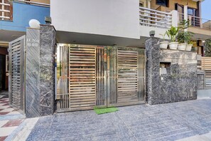 A gated entrance with a marble facade, a metal gate, and a small green mat on the ground. - Hotel O Premier Stays (Gurugram)