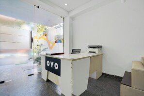 A reception desk with a sign that reads 'OYO' in a modern office setting with a glass partition and a view of the outside. - Hotel O Premier Stays (Gurugram)
