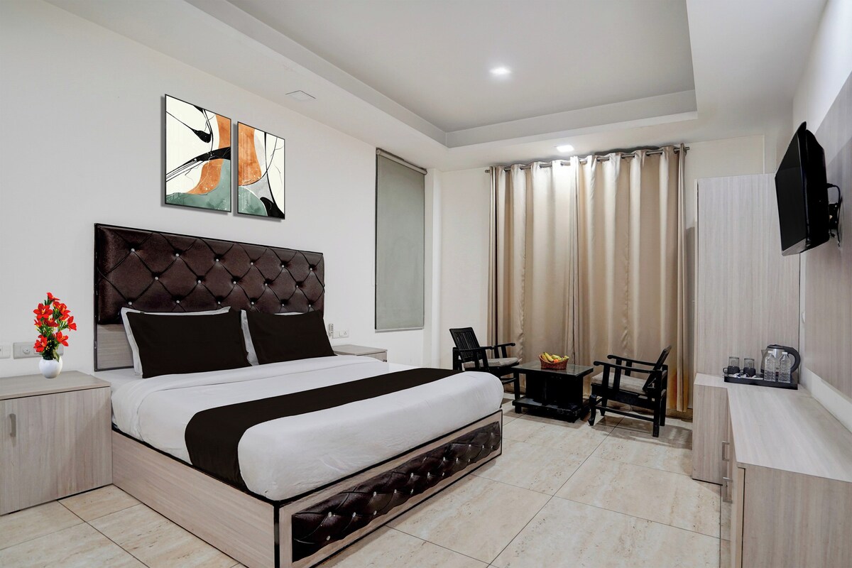 Una habitación de hotel moderna con una cama grande, un televisor de pantalla plana, un escritorio con una silla y un ventanal con cortinas.