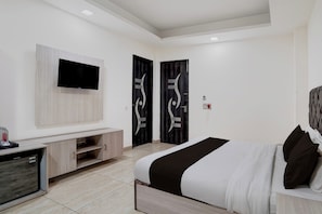 Una habitación de hotel moderna con un televisor de pantalla plana montado en la pared, una cama con colcha blanco y negro, y un mueble bajo para televisión de madera con un televisor de pantalla plana y un minibar.