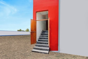 Un edificio con fachada roja, una puerta de madera y una escalera que conduce a un interior oscuro.