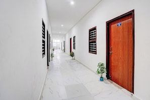 Un pasillo con paredes blancas, puertas de madera y plantas en macetas.