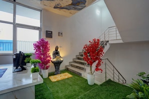 Un interior moderno con una escalera, follaje artificial y una estatua de Buda.