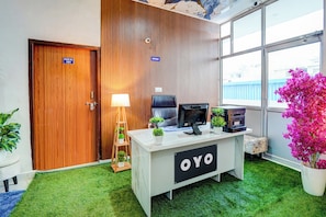 Una oficina con escritorio, computadora y plantas. Hay una puerta con la etiqueta 'ROOM NO. 101' y un letrero que indica 'OFFICE'.
