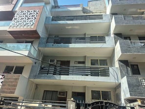 Un edificio residencial de varios pisos con balcones, ventanas y una entrada protegida por un portón.