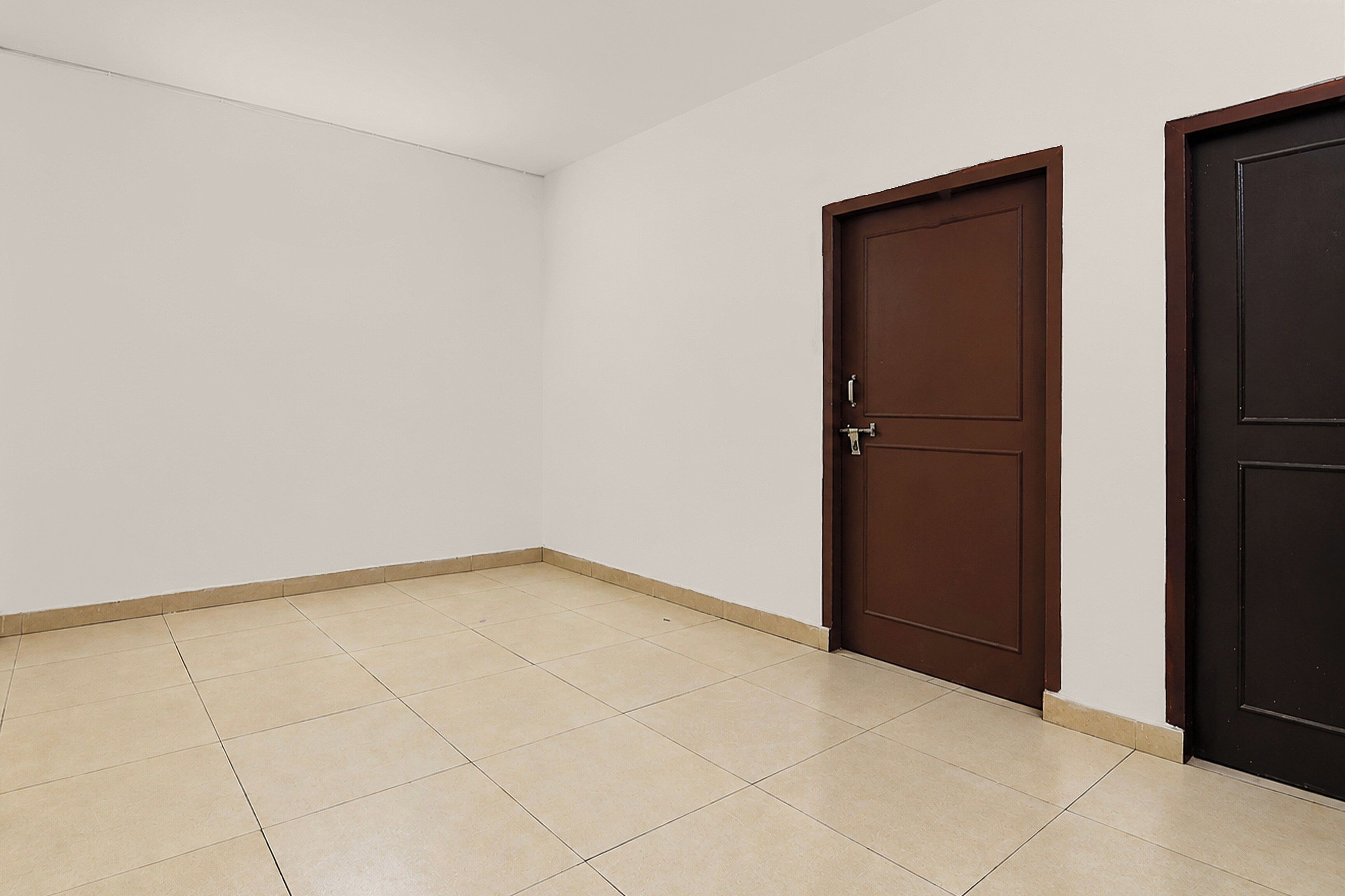 Een kamer met een betegelde vloer, twee gesloten deuren en effen witte muren.