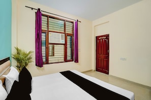 A hotel room with a bed, a window with curtains, a door, and a potted plant. - Hotel O Shivik Stays (Gurugram)