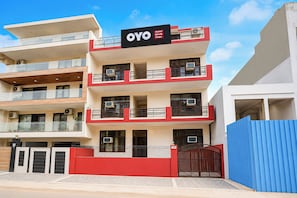 A multi-story hotel building with balconies, air conditioning units, and a red and white color scheme. - Hotel O Shivik Stays (Gurugram)