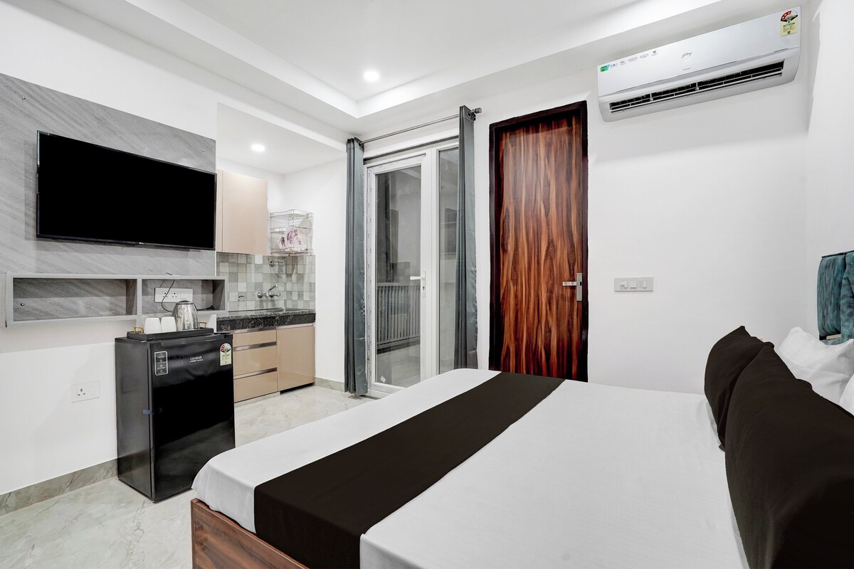 A modern bedroom with a bed, a TV, a kitchen area, and an air conditioning unit.
