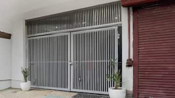 Una reja metálica cerrada con diseño de barras verticales, una puerta de garaje roja y dos macetas con plantas en el suelo.