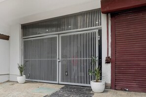 Una reja metálica cerrada con diseño de barras verticales, una puerta de garaje roja y dos macetas con plantas en el suelo.