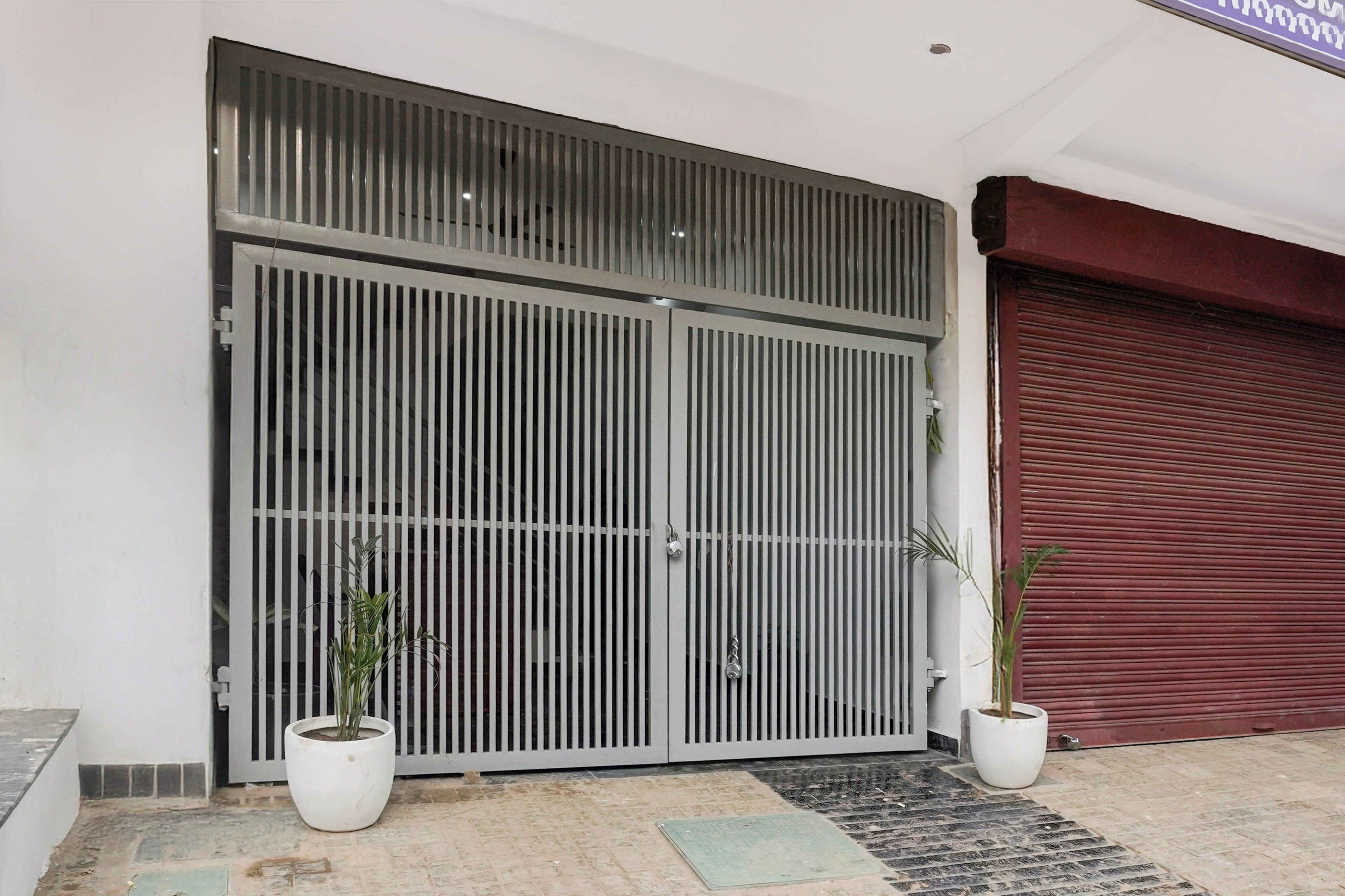 Una entrada protegida por un portón metálico, con dos plantas en macetas y un acceso con contraventanas rojas.