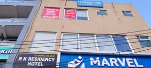 A building with multiple signs advertising R K Residency Hotel, including availability of luxury rooms, 24x7 AC rooms, and amenities like breakfast, lunch, dinner, and parking. - Hotel O R K Residency (Gurugram)