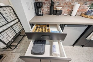 A kitchen with a drawer containing utensils, a coffee maker, and a tea set. - SoHo Vibes - EaDo Lofts #B (Houston)