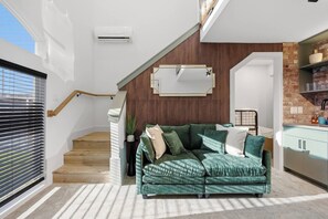 A modern living room with a green sectional sofa, a staircase, and a kitchen area. - SoHo Vibes - EaDo Lofts #A (Houston)