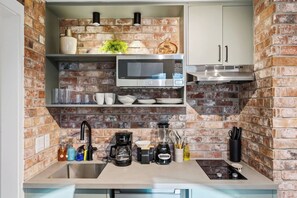 A compact kitchen with a brick backsplash, a microwave, a coffee maker, and a small sink. - SoHo Vibes - EaDo Lofts #A (Houston)