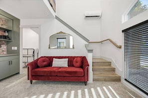 A red sofa in a modern living area with a staircase and a window with blinds. - SoHo Vibes - EaDo Lofts #1 (Houston)