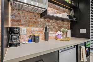 A kitchen with a brick backsplash, a coffee maker, a tea set, and a basket with a gift. - SoHo Vibes - EaDo Lofts #2 (Houston)