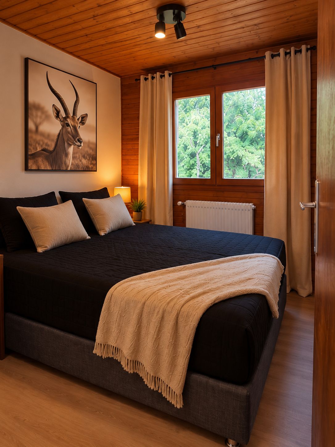 A bedroom with a large bed, wooden ceiling, a window with curtains, and a wall-mounted lamp.