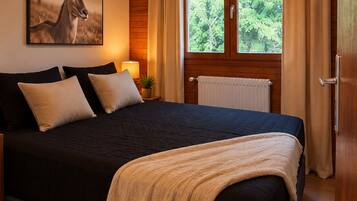 A bedroom with a large bed, wooden ceiling, a window with curtains, and a wall-mounted lamp.