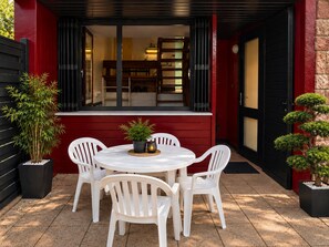 A patio with a round table and white chairs, surrounded by potted plants. - New Listing (Albé)