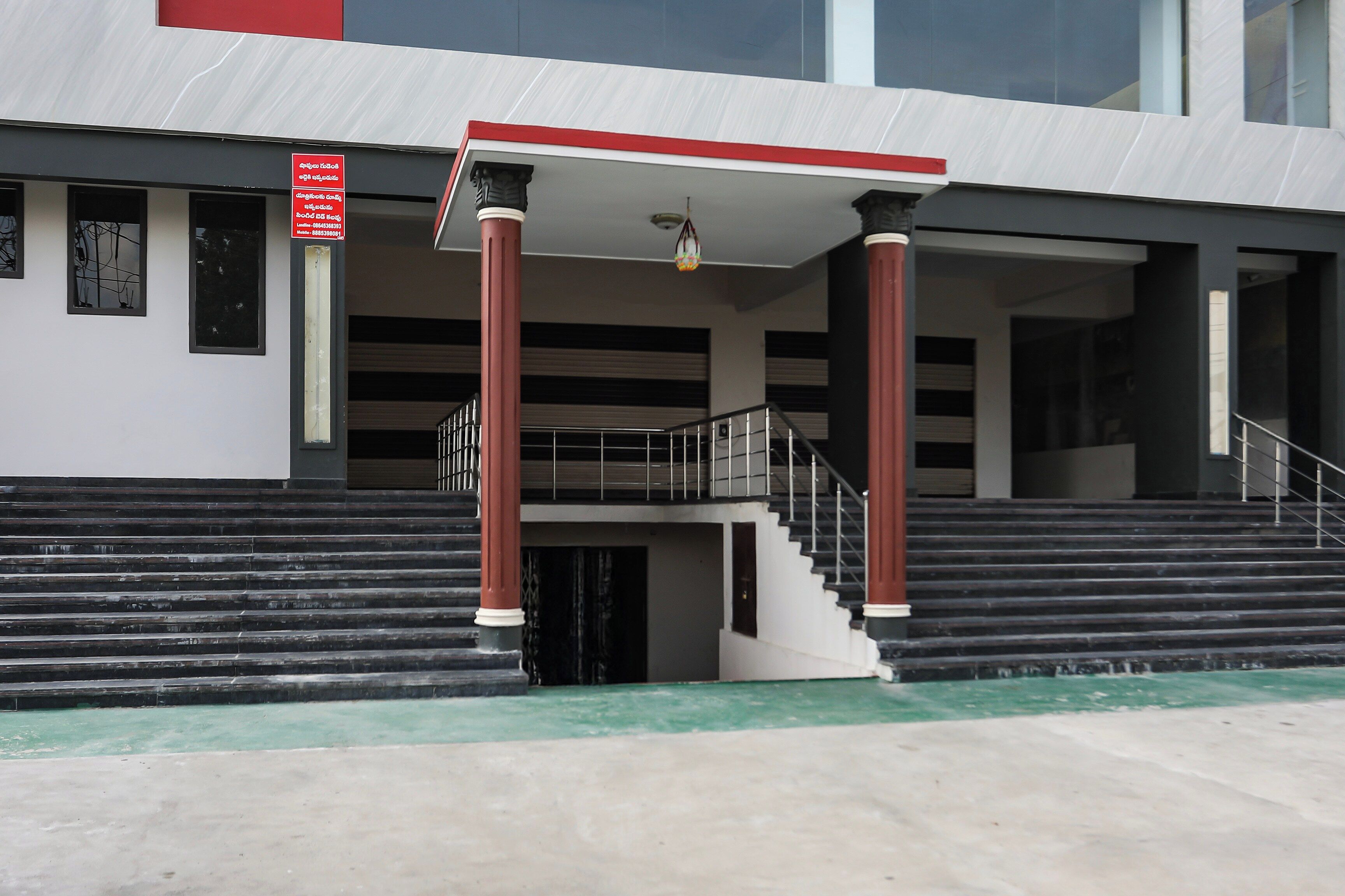 A building entrance with a covered staircase, a red and white sign, and a modern architectural design.