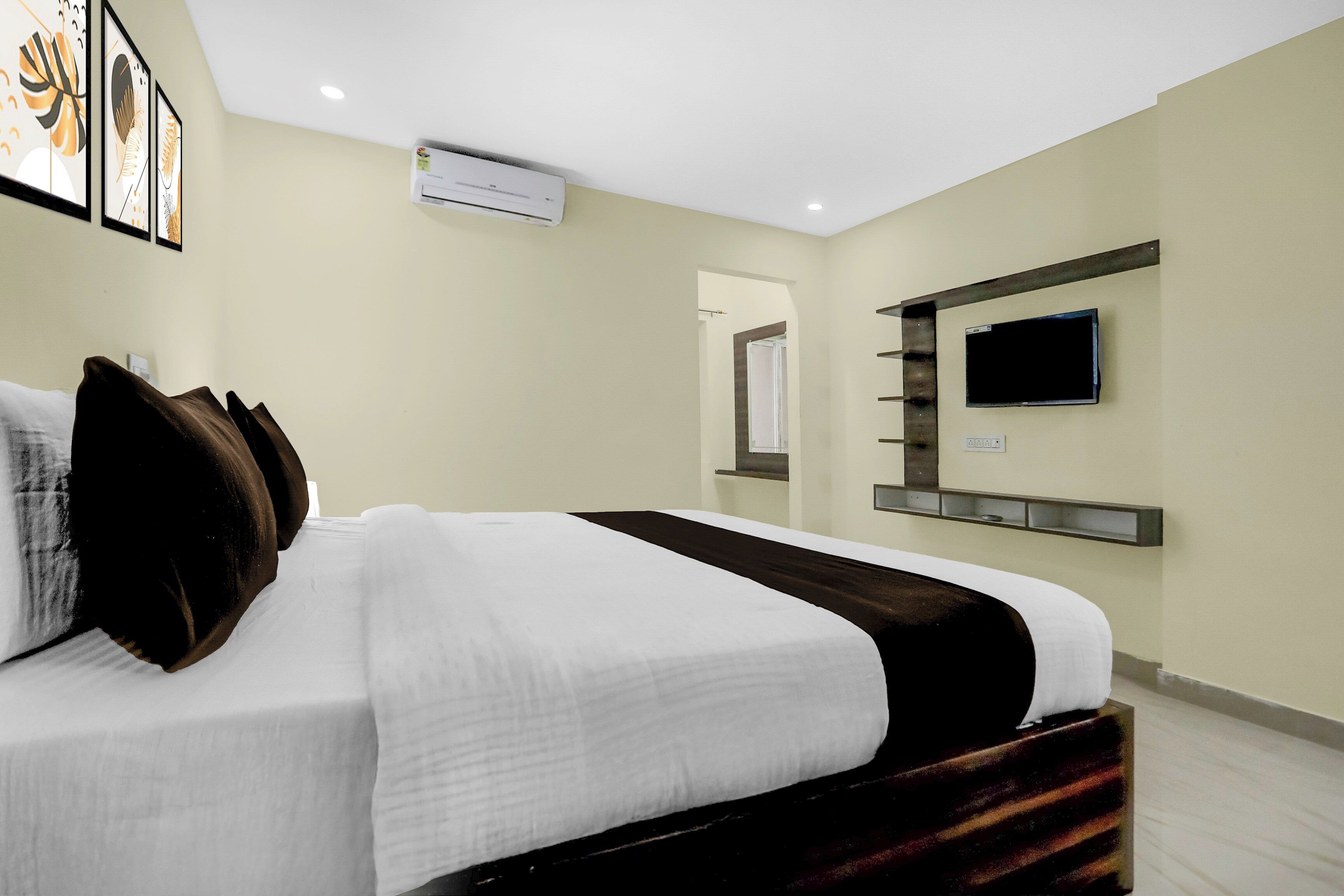 A hotel room with a bed, a flat-screen TV mounted on the wall, and an air conditioning unit.