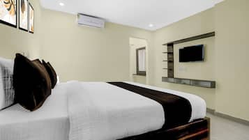 A hotel room with a bed, a flat-screen TV mounted on the wall, and an air conditioning unit.