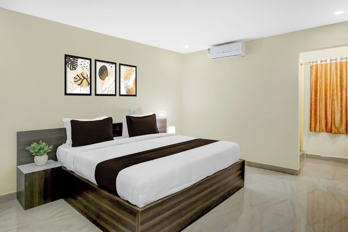 A hotel room with a bed, a nightstand, a potted plant, and artwork on the wall.