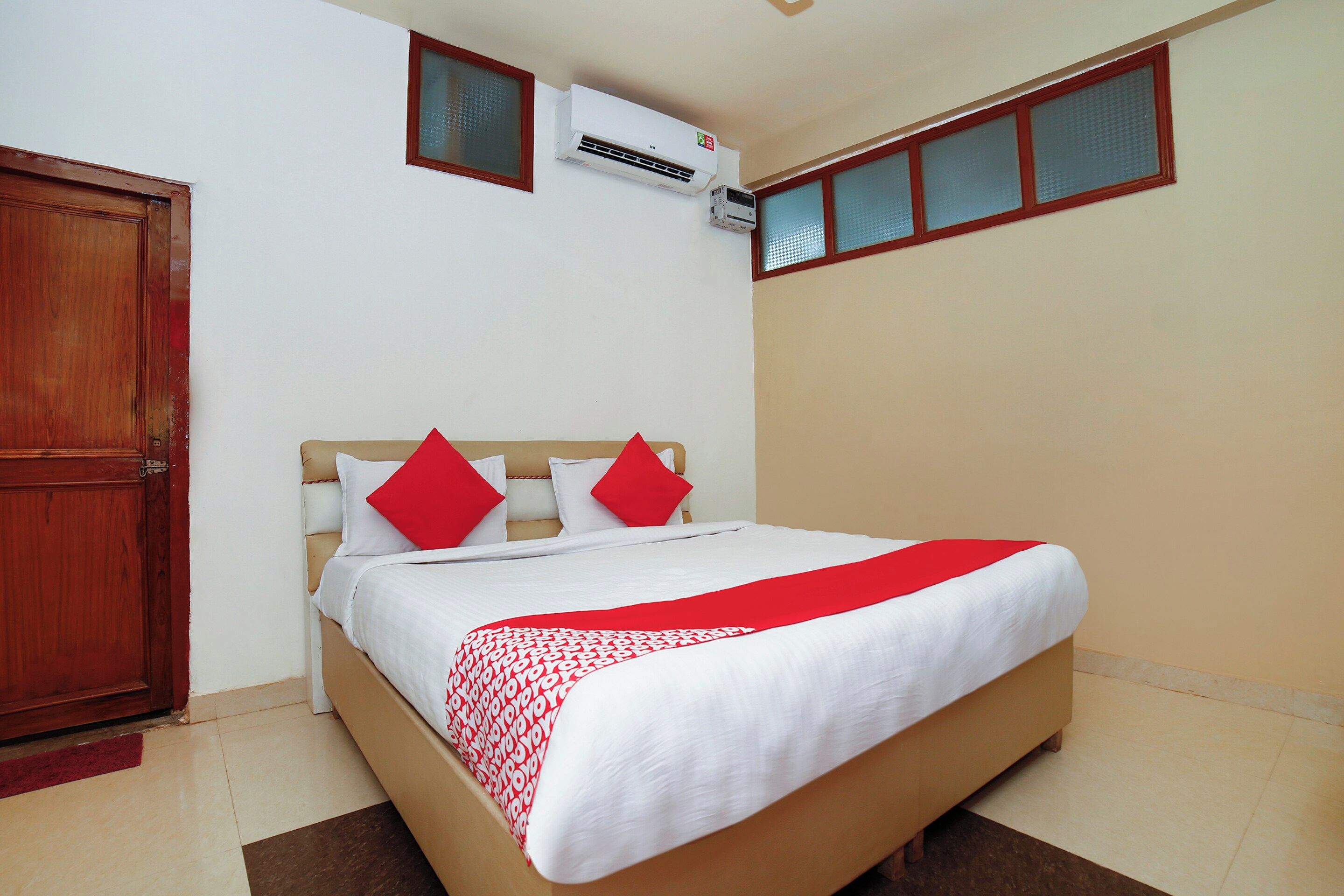 A hotel room with a bed, a wooden door, an air conditioning unit, and a window with a view.