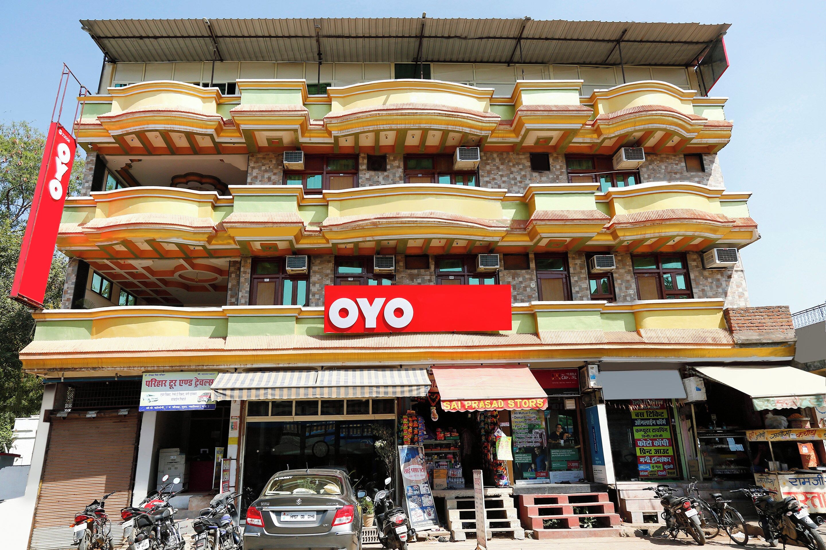 A multi-story building with a prominent red 'OYO' sign, multiple balconies, and a ground-level shop with a striped awning.
