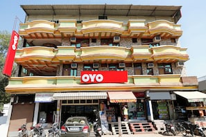 A multi-story building with a prominent red 'OYO' sign, multiple balconies, and a ground-level shop with a striped awning. - Hotel O Rama Utsav (Gwalior)