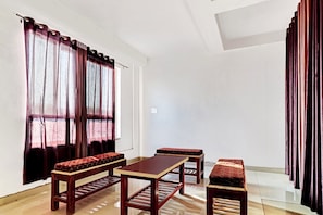 A room with a wooden table and benches, large windows with curtains, and a tiled floor. - Hotel O Royal (Gwalior)