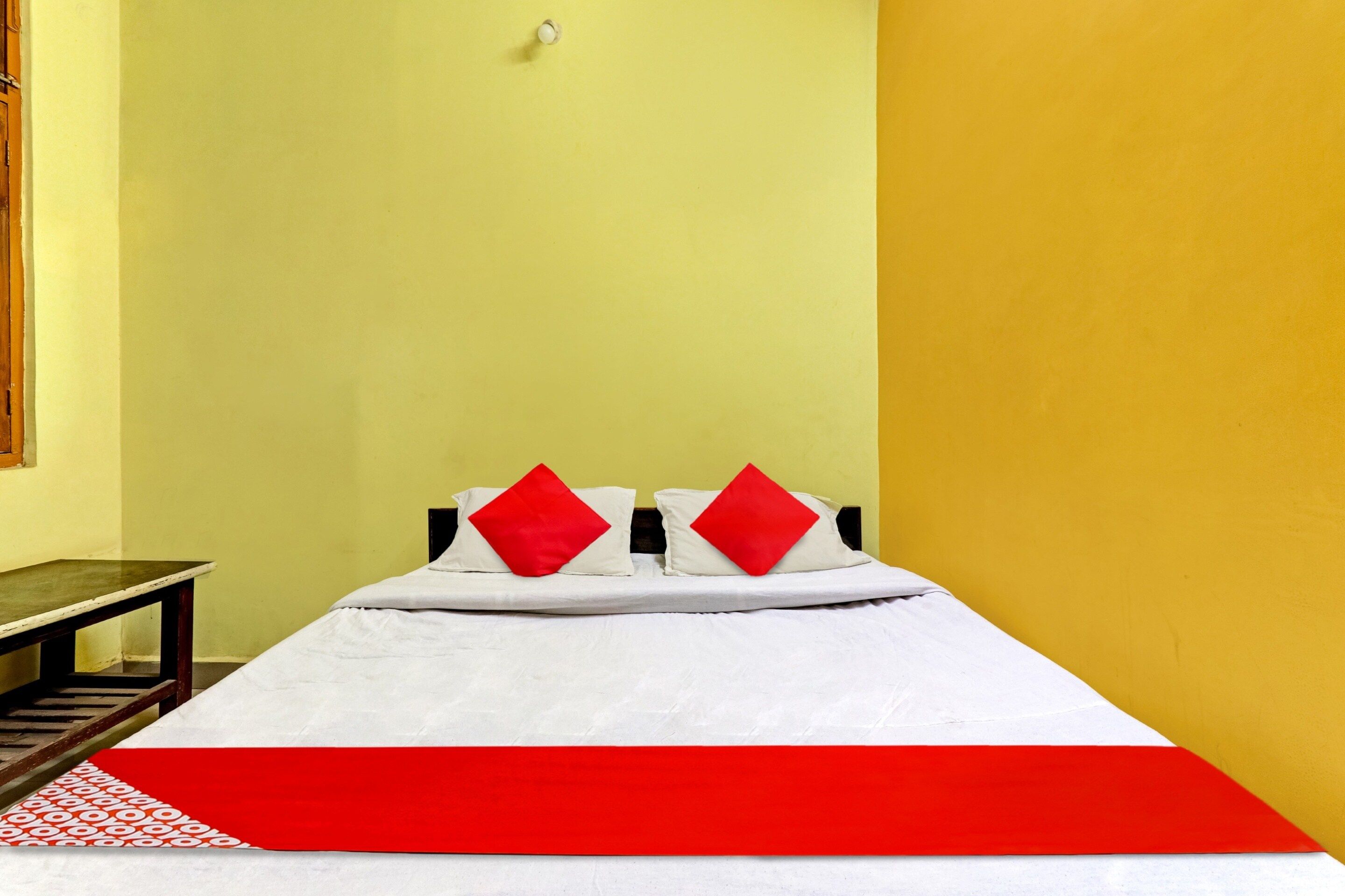 A bed with white bedding and two red pillows, a red and white striped area rug, and a wooden nightstand.