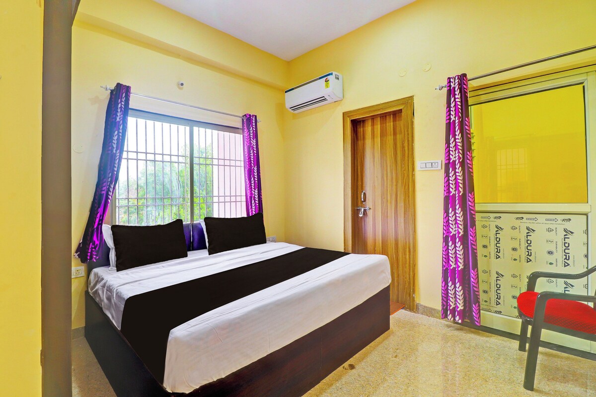 Un dormitorio con cama, ventana con cortinas, unidad de aire acondicionado, puerta y una silla.