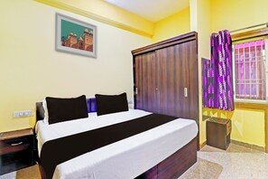 Habitación de hotel con cama, armario, mesita de noche, ventana con cortinas y un interruptor de luz en la pared.