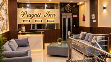 Zona de recepción del Pragati Inn con mostrador, asientos de sala y una escalera.