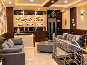 Zona de recepción del Pragati Inn con mostrador, asientos de sala y una escalera.