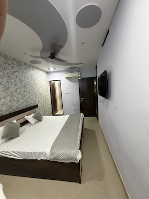 A bedroom with a bed, a wall-mounted TV, and a ceiling fan. - Hotel PRAGATI INN (Kanpur)