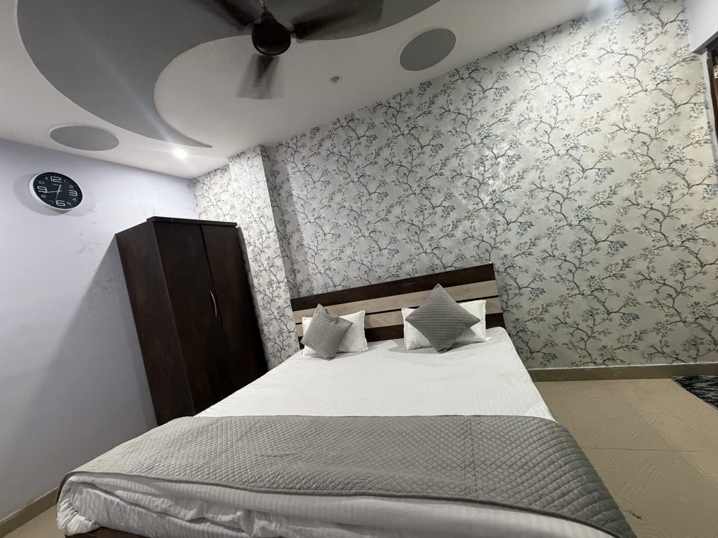 A bedroom with a bed, a wardrobe, a ceiling fan, and a clock on the wall.