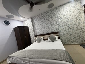 A bedroom with a bed, a wardrobe, a ceiling fan, and a clock on the wall. - Hotel PRAGATI INN (Kanpur)